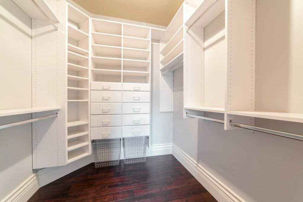 Fitted wardrobe interior with white shelving, drawers, and hanging space, showcasing bespoke woodwork and custom furniture solutions.