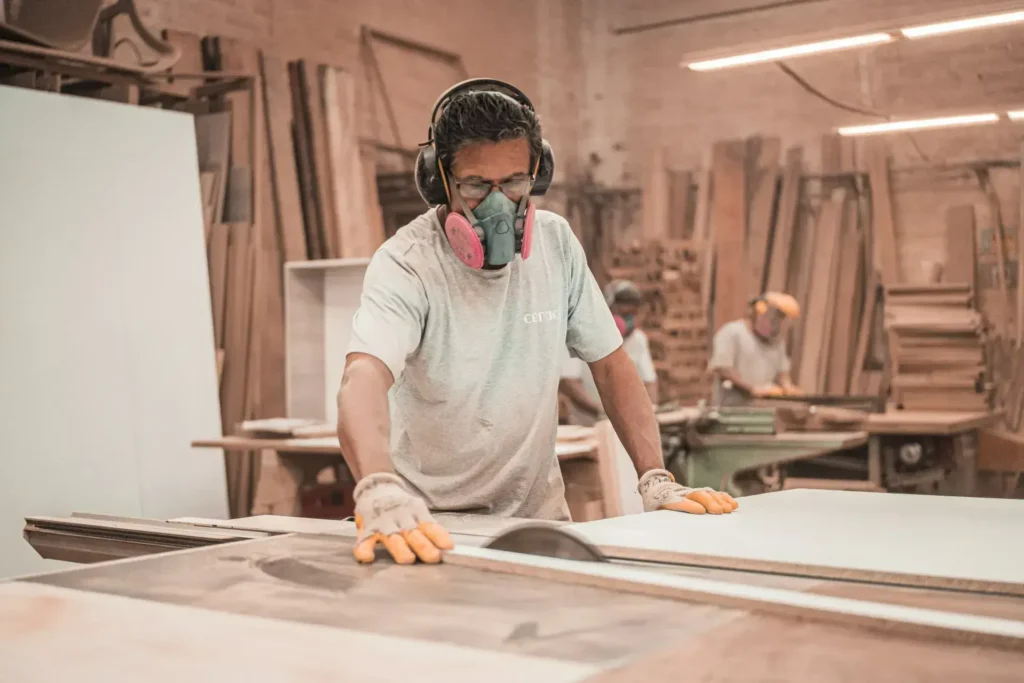 Man using woodworking equipment in a workshop, wearing protective gear, focused on crafting bespoke fitted furniture and joinery.