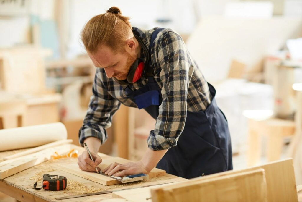 Carpenter measuring and marking wood for bespoke joinery in a workshop setting, highlighting craftsmanship in carpentry and fitted furniture.